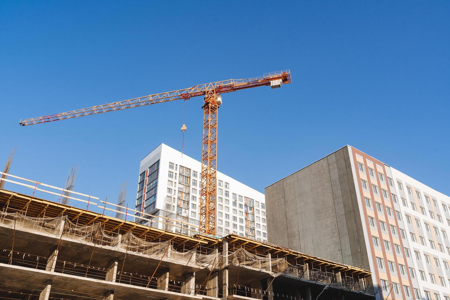 A crane builds a house, a yellow hoist participates in the construction of a residential building, lifting heavy loads to a height. photo