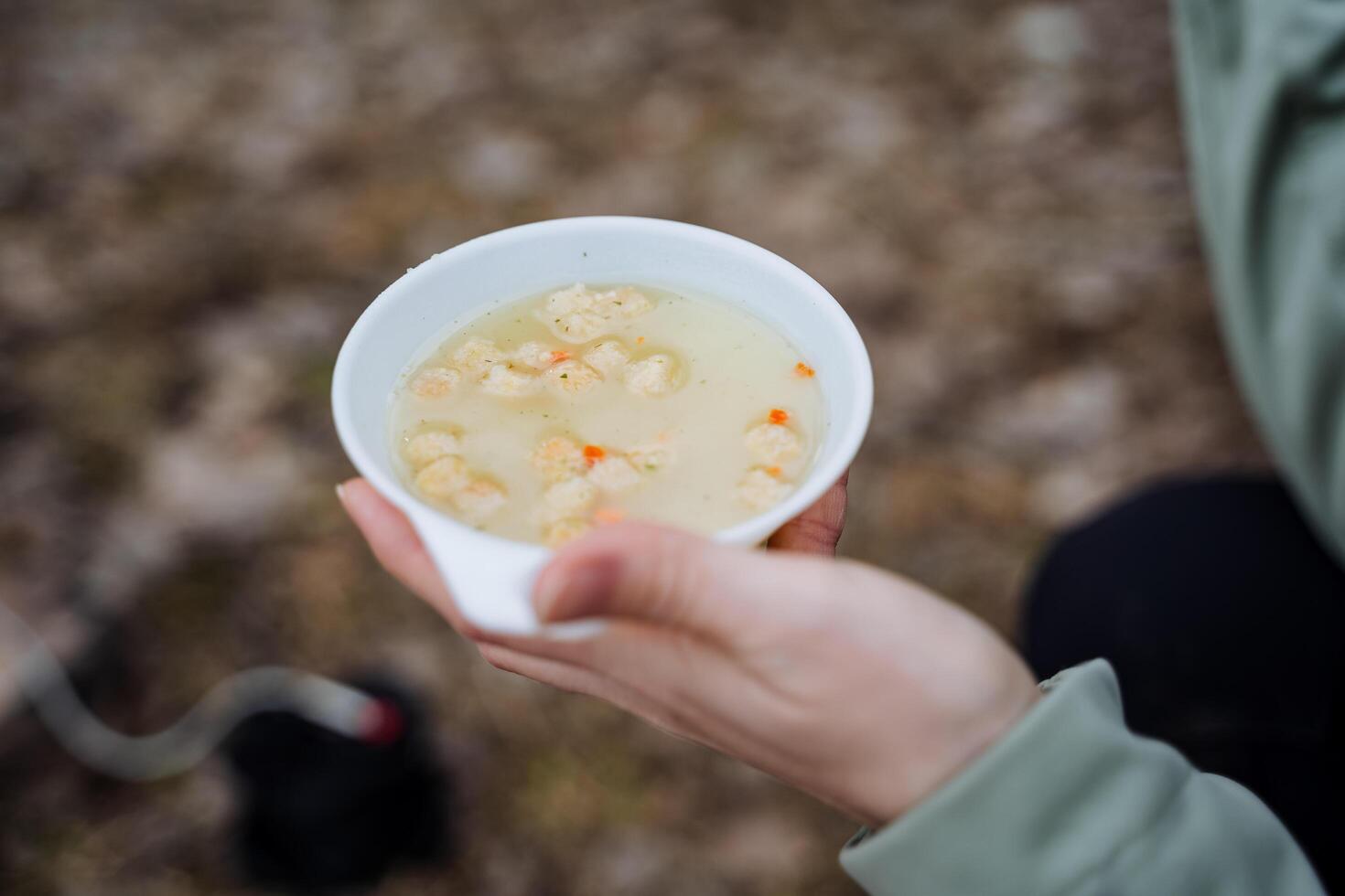 A bowl of soup in hand, a quick meal, a camper's lunch, mashed breadcrumbs, liquid food, a white plate. photo