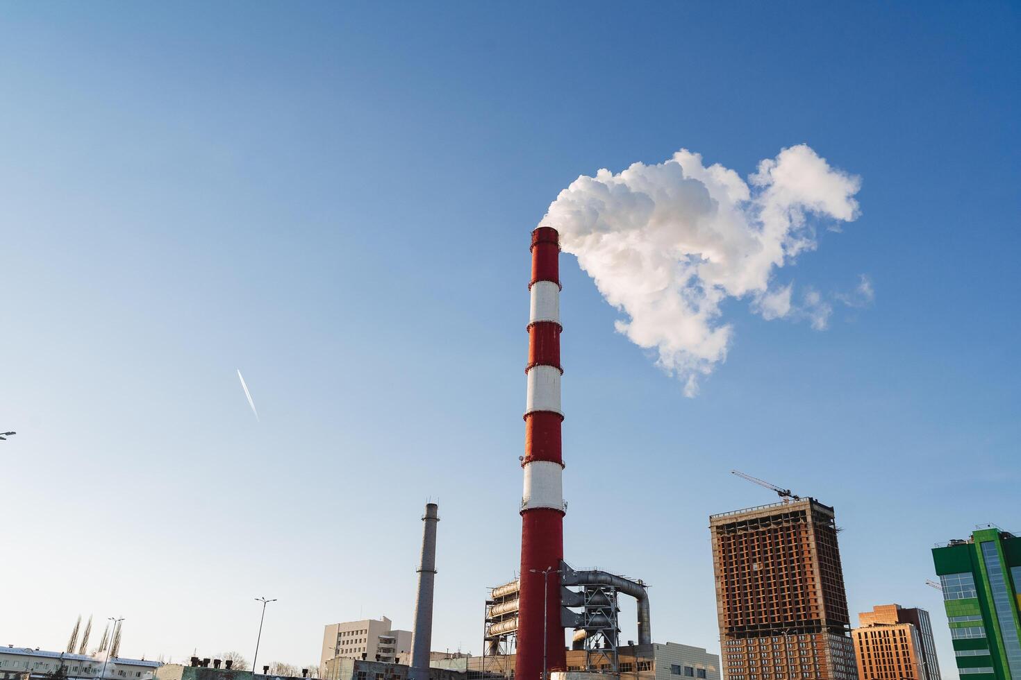 The city is polluted by harmful emissions coming out of the pipes of the plant. The carbon footprint falls on buildings, climate warming, a pipe against the sky. photo