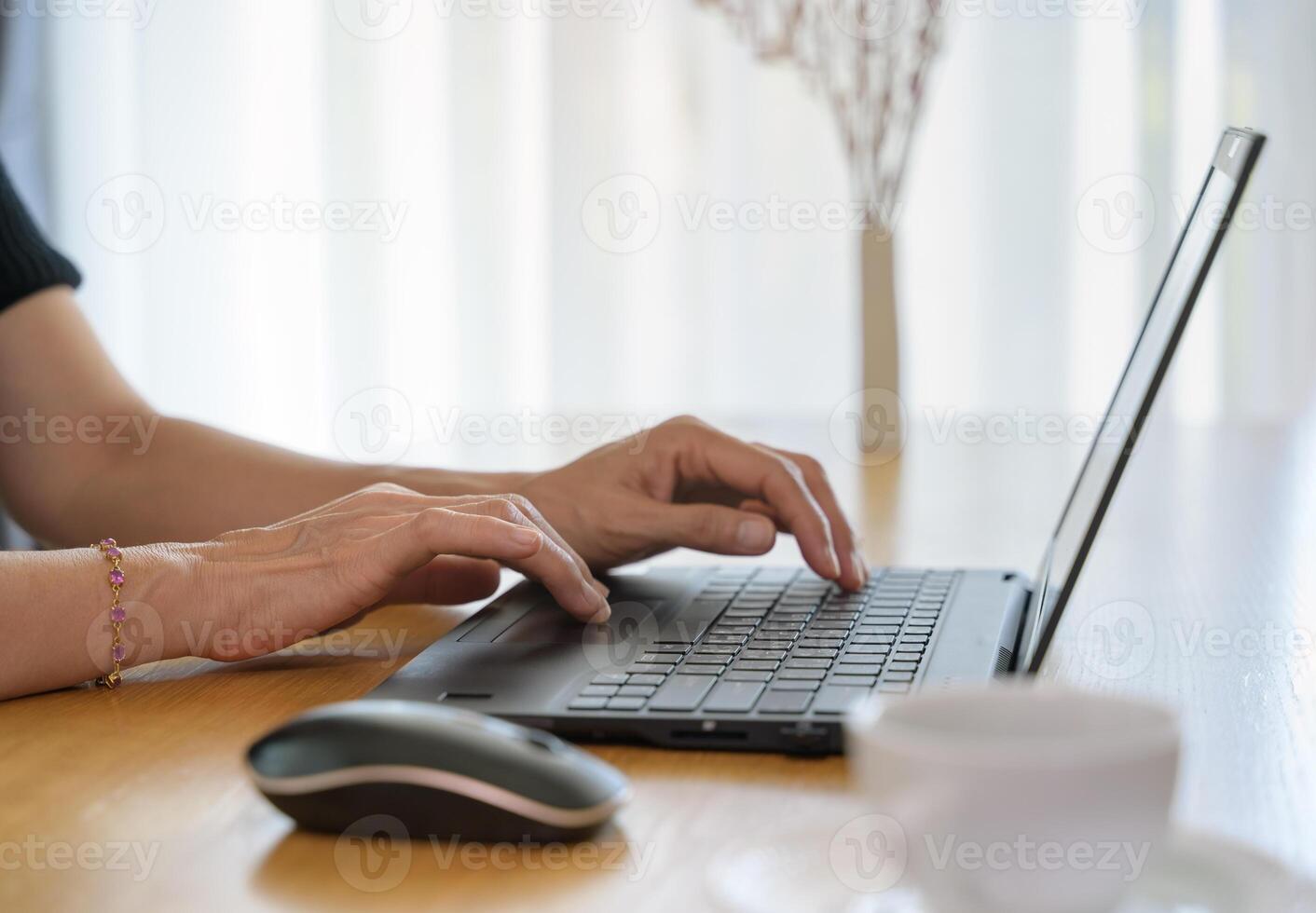 Close up of woman hands working with laptop while sitting at desk with a cup of coffee at home photo