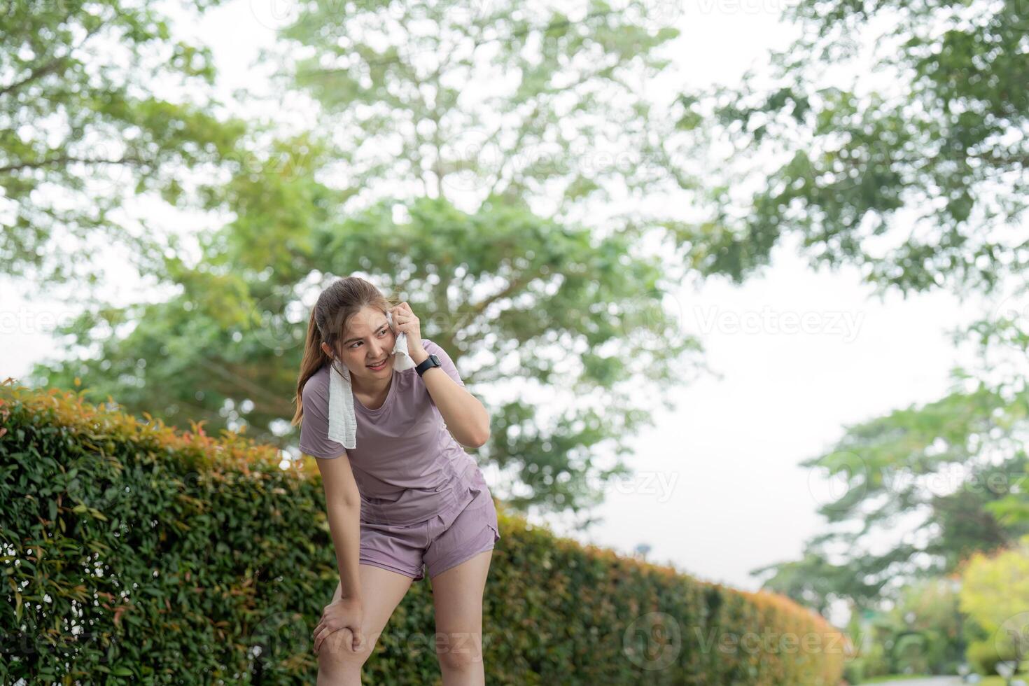 Asian woman taking a moment to catch her breath after tired workout in park photo