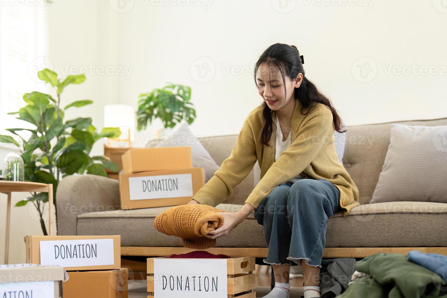 Woman asian holding donation box full with clothes and select clothes. Concept of donation and clothes recycling. Helping poor people photo