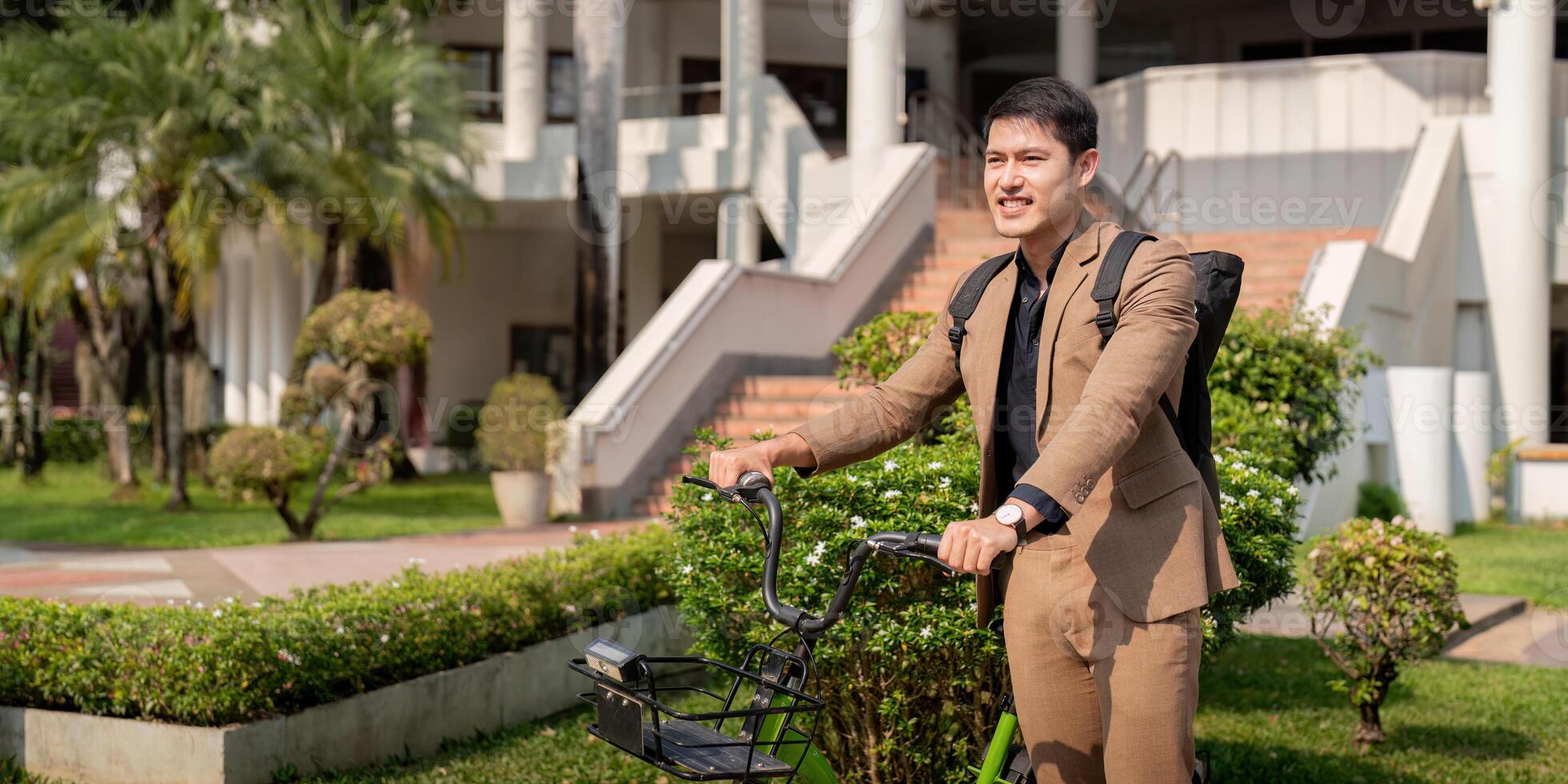 Asian businessman in a suit is riding a bicycle on the city streets for his morning commute to work. Eco transportation concept, sustainable lifestyle concept photo