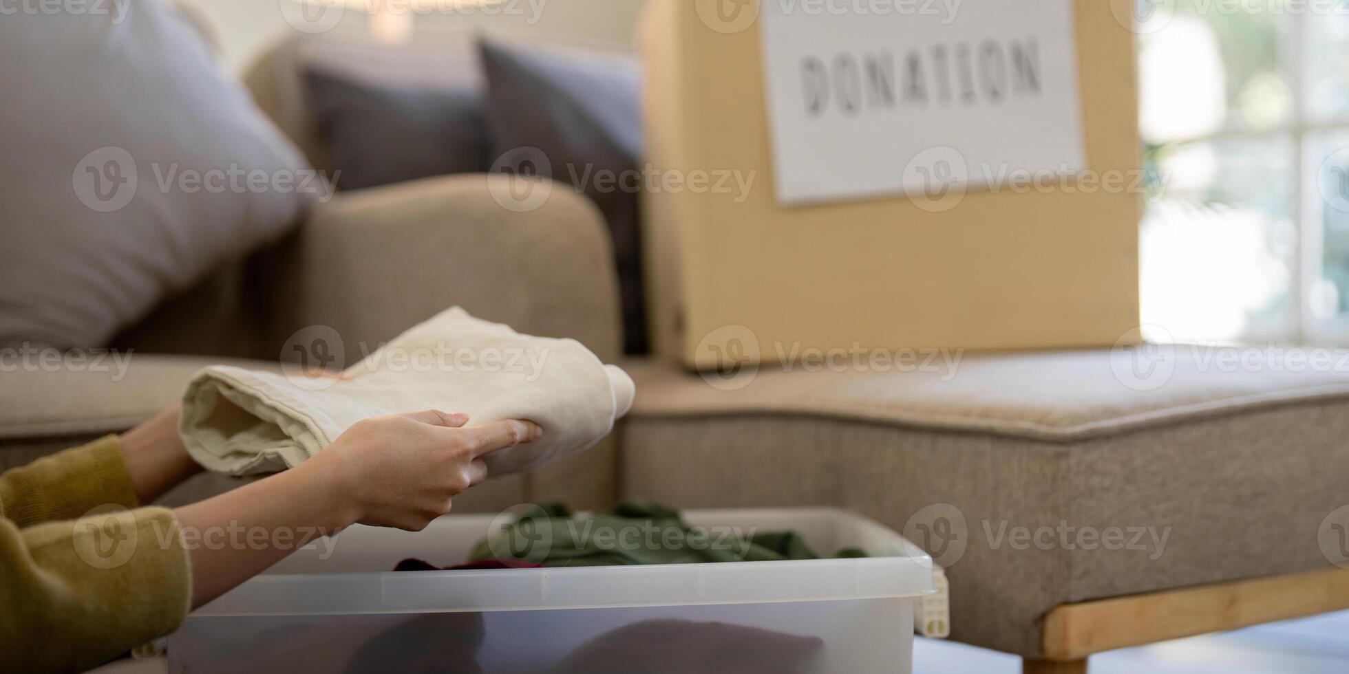 Donation, asian young woman sitting pack object at home, putting on stuff into donate box with second hand clothes, charity helping and needy people. Reuse recycle photo