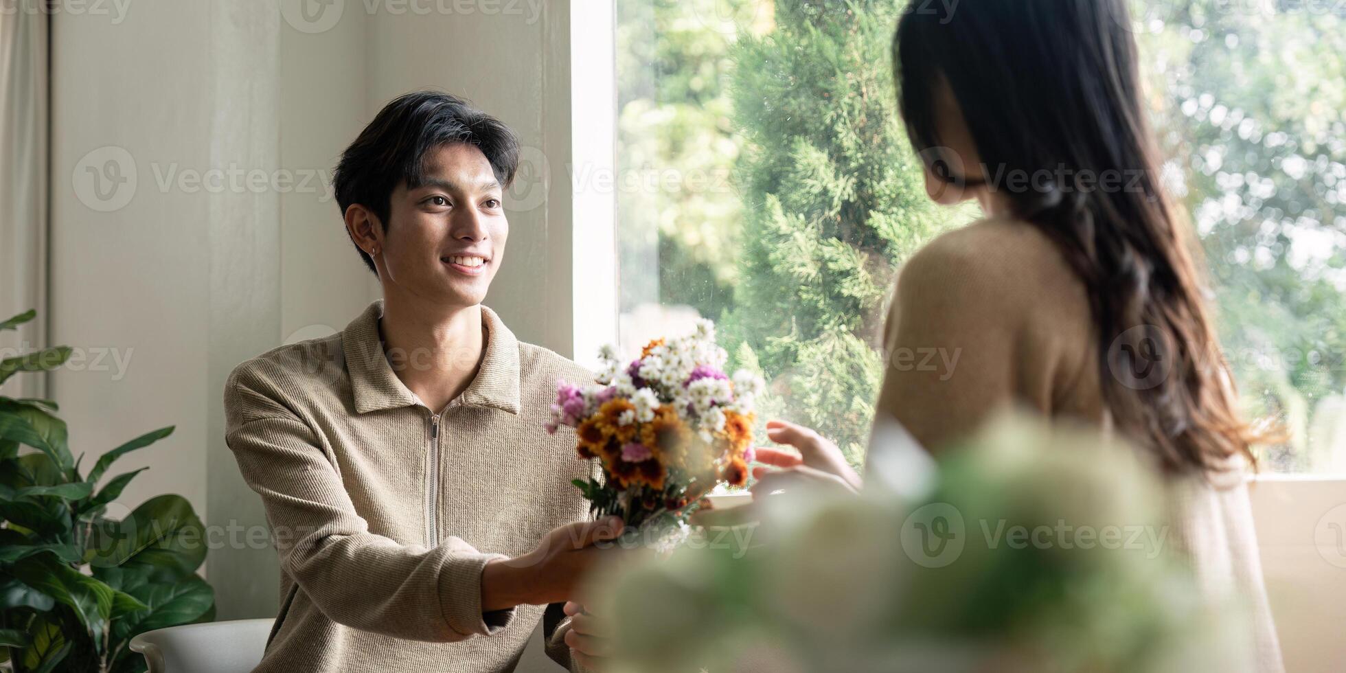 Romantic young asian couple embracing with holding flowers and smiling in living room at home. fall in love. Valentine concept photo