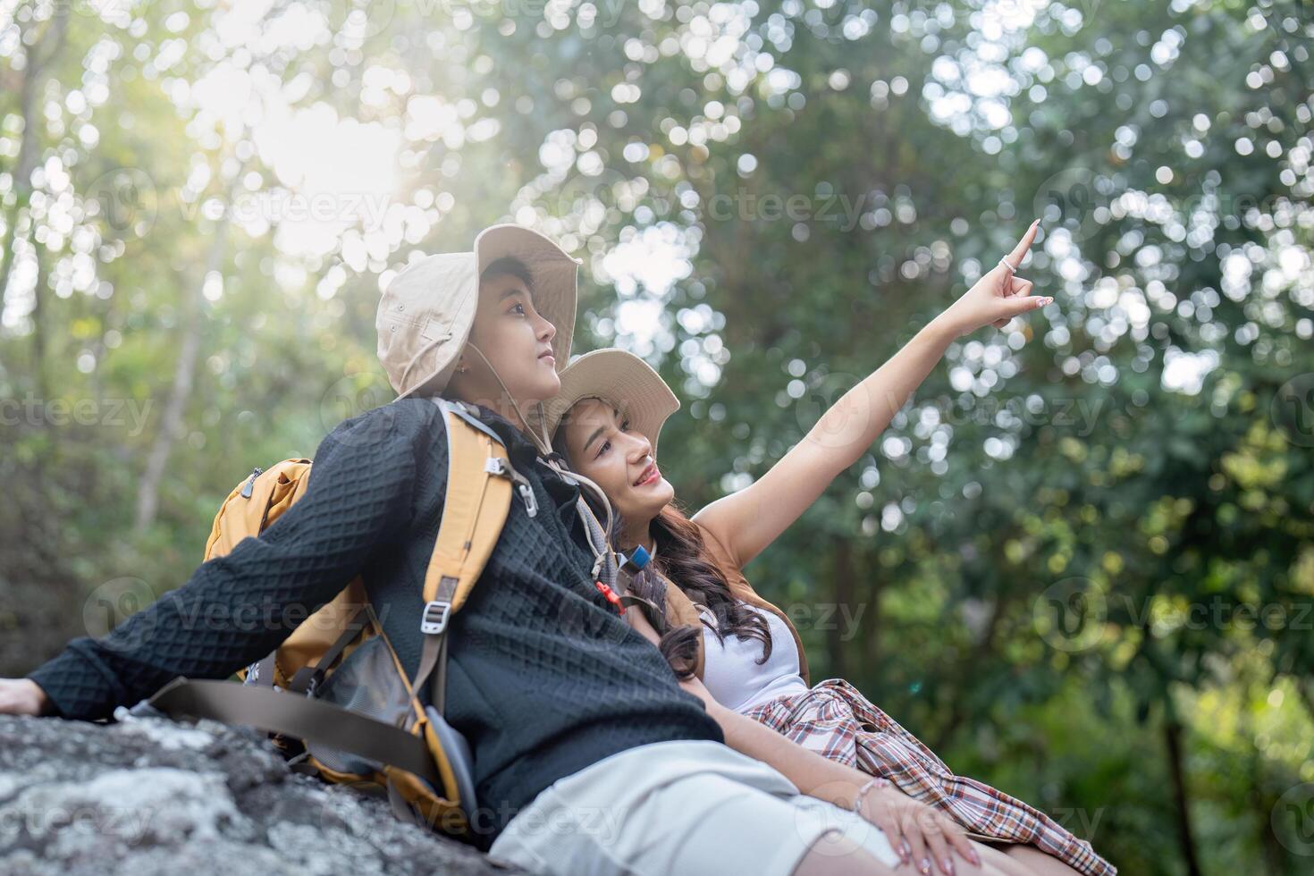Cheerful romantic lesbian couple traveler with backpacks on their backs go hiking through the forest and siting relaxing while hiking in the mountains in summer photo