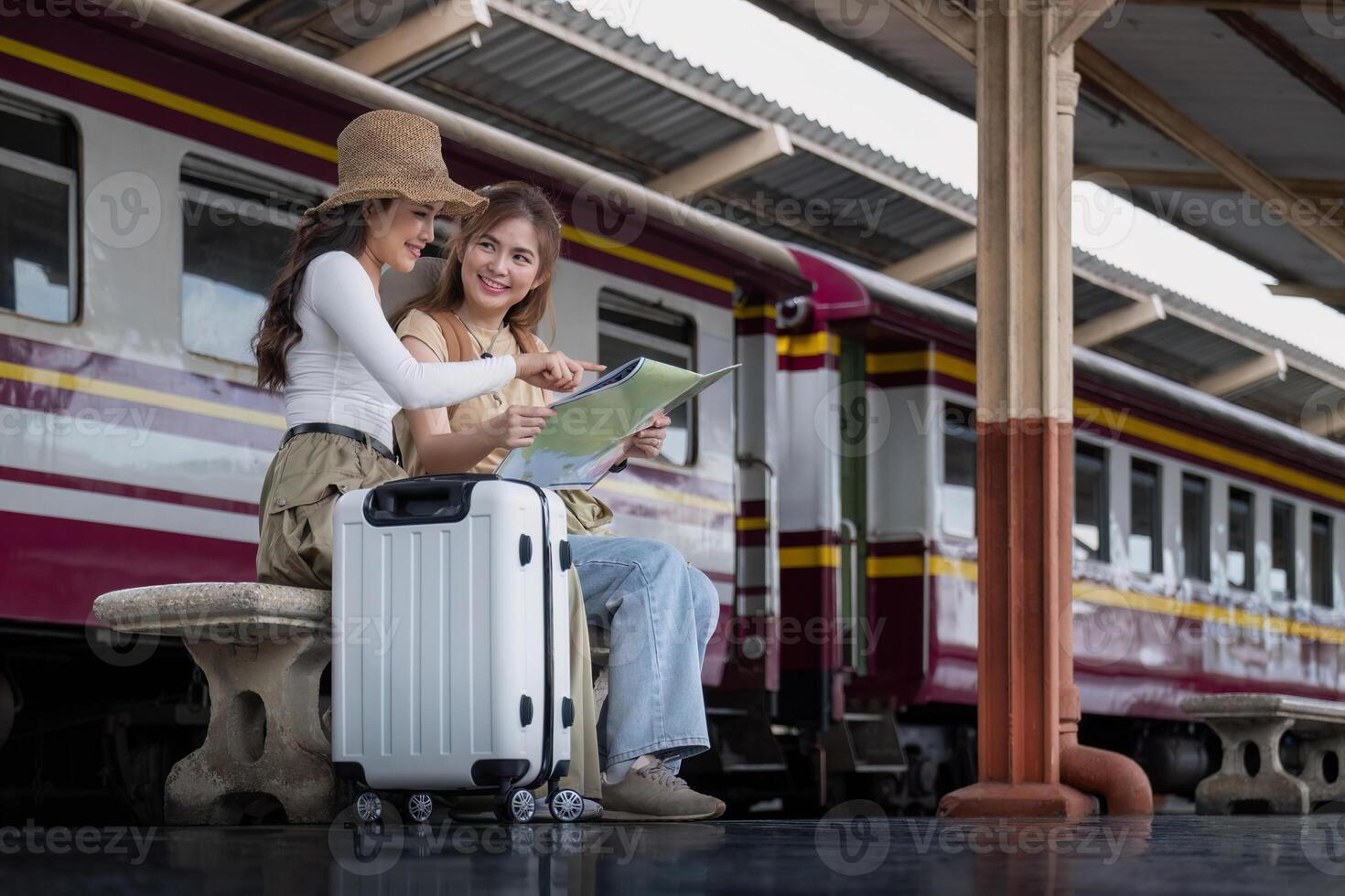 viaje concepto. niña amigo vestir sombrero participación mapa tener bolso y equipaje. hembra viajero esperando tren a tren estación foto