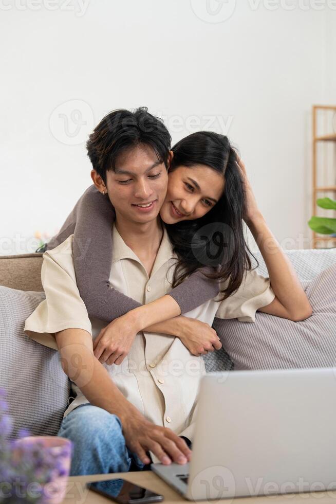 Happy asian couple using laptop sit relax on sofa doing ecommerce shopping online on website at home photo