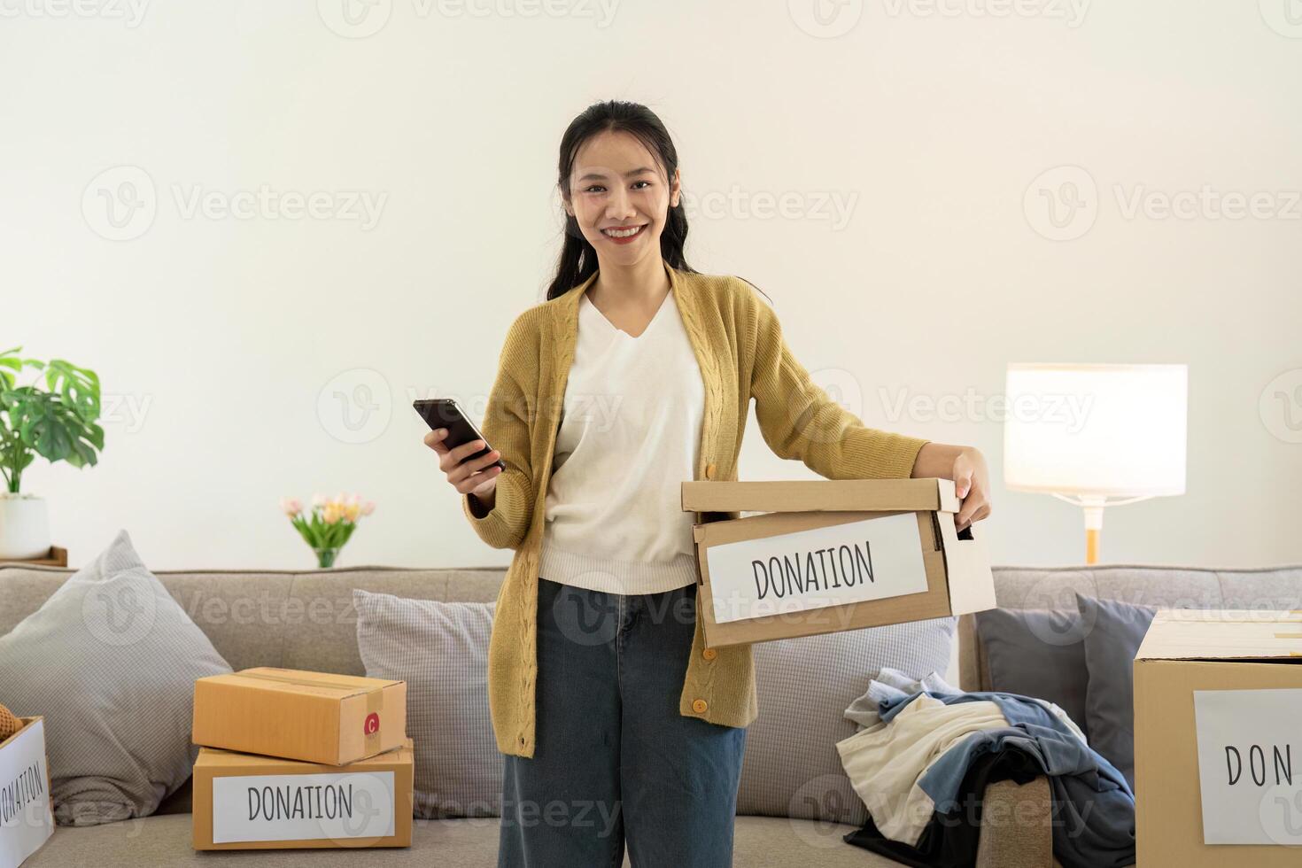 donación concepto. mujer asiático participación un donar caja con lleno de ropa. mujer participación ropa donar caja. ropa en caja para concepto donación y reutilizar reciclar foto