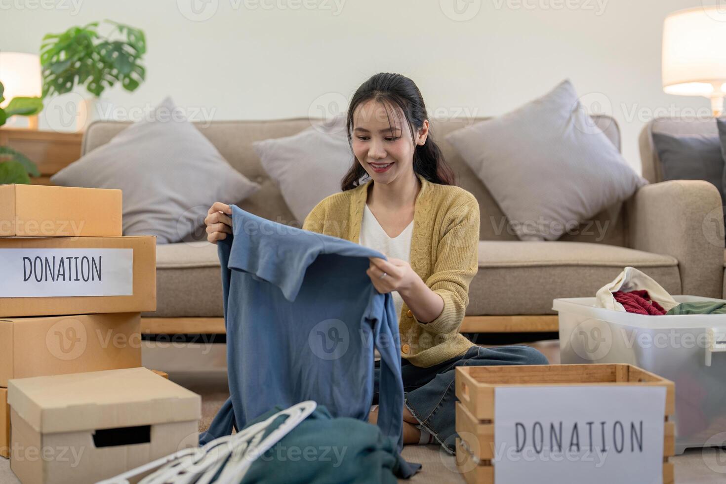 Woman asian holding donation box full with clothes and select clothes. Concept of donation and clothes recycling. Helping poor people photo