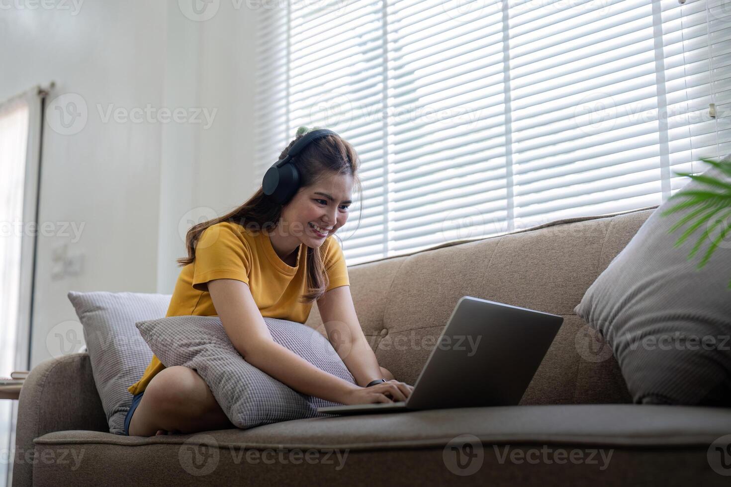 Happy woman wearing headphones watching and listening video on laptop and listening music sitting on a couch at home photo