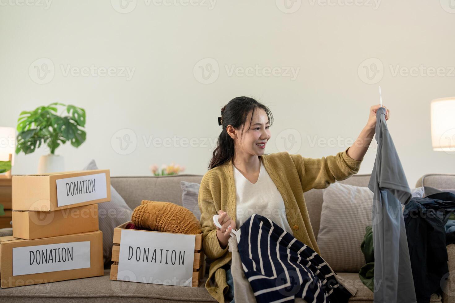 Woman asian holding donation box full with clothes and select clothes. Concept of donation and clothes recycling. Helping poor people photo