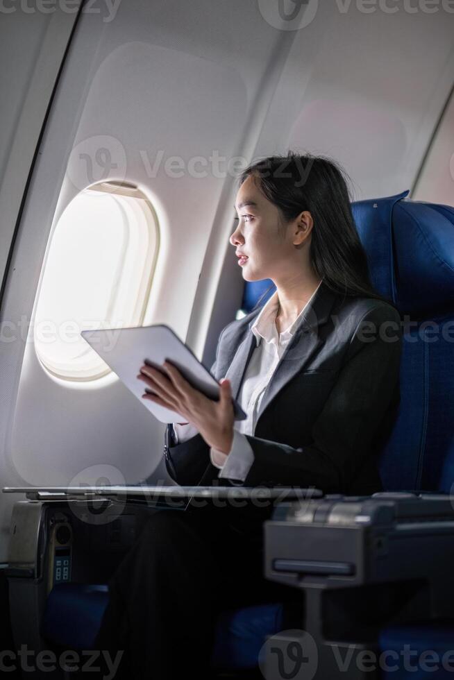 Successful young asian business woman sits in airplane cabin plane and working from anywhere. Flying at first class photo