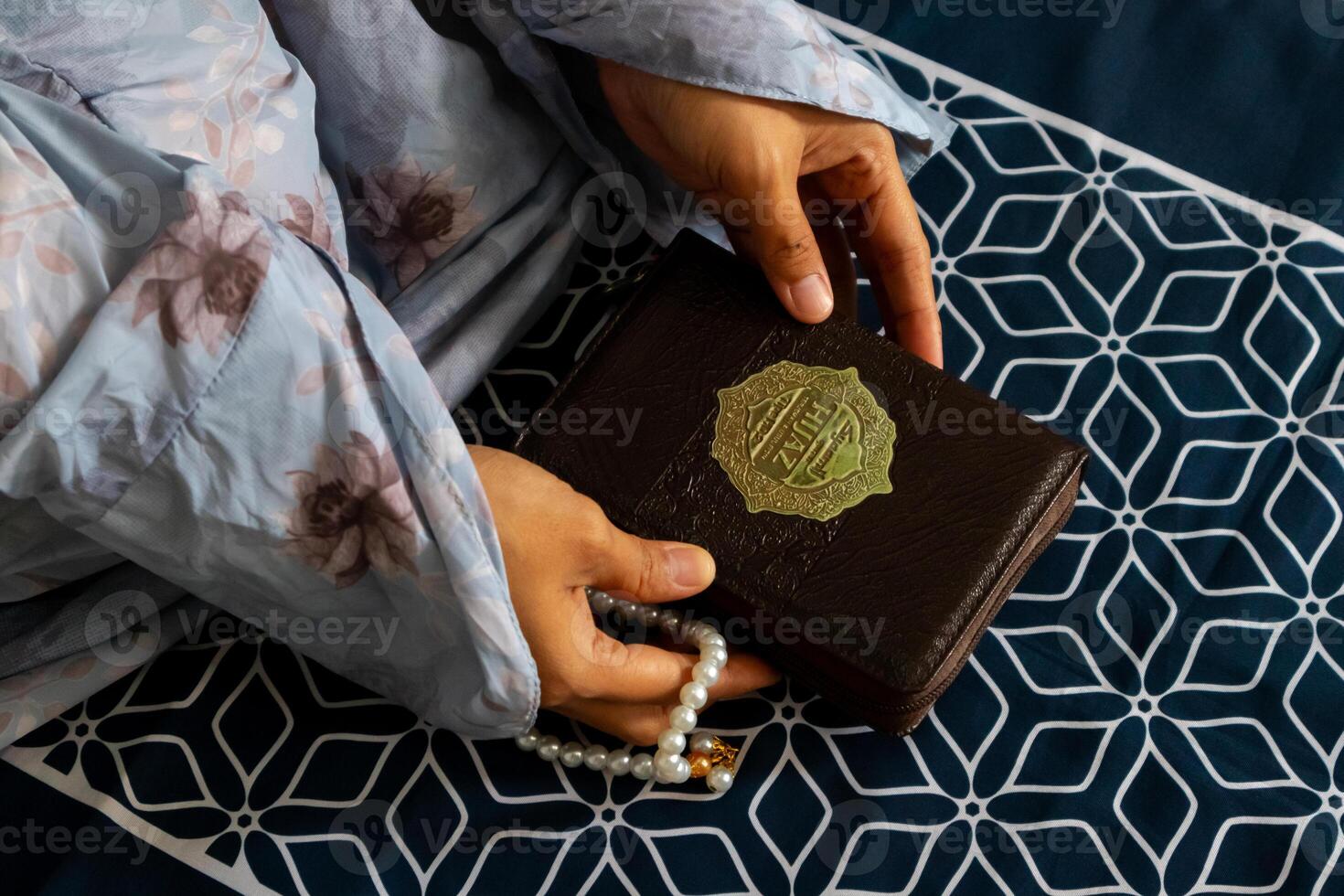 un musulmán mujer sentado en un oración estera y participación el Corán con indonesio Traducción foto