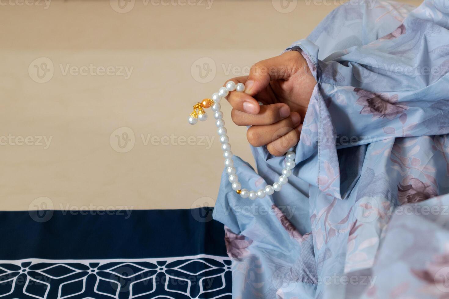 A Muslim woman wearing a moslem clothes with hijab called mukena and holding prayer beads for praying or dhikr photo