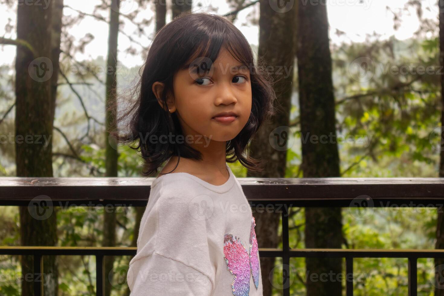 An Asian little girl standing and posing on the balcony with nature or trees background photo