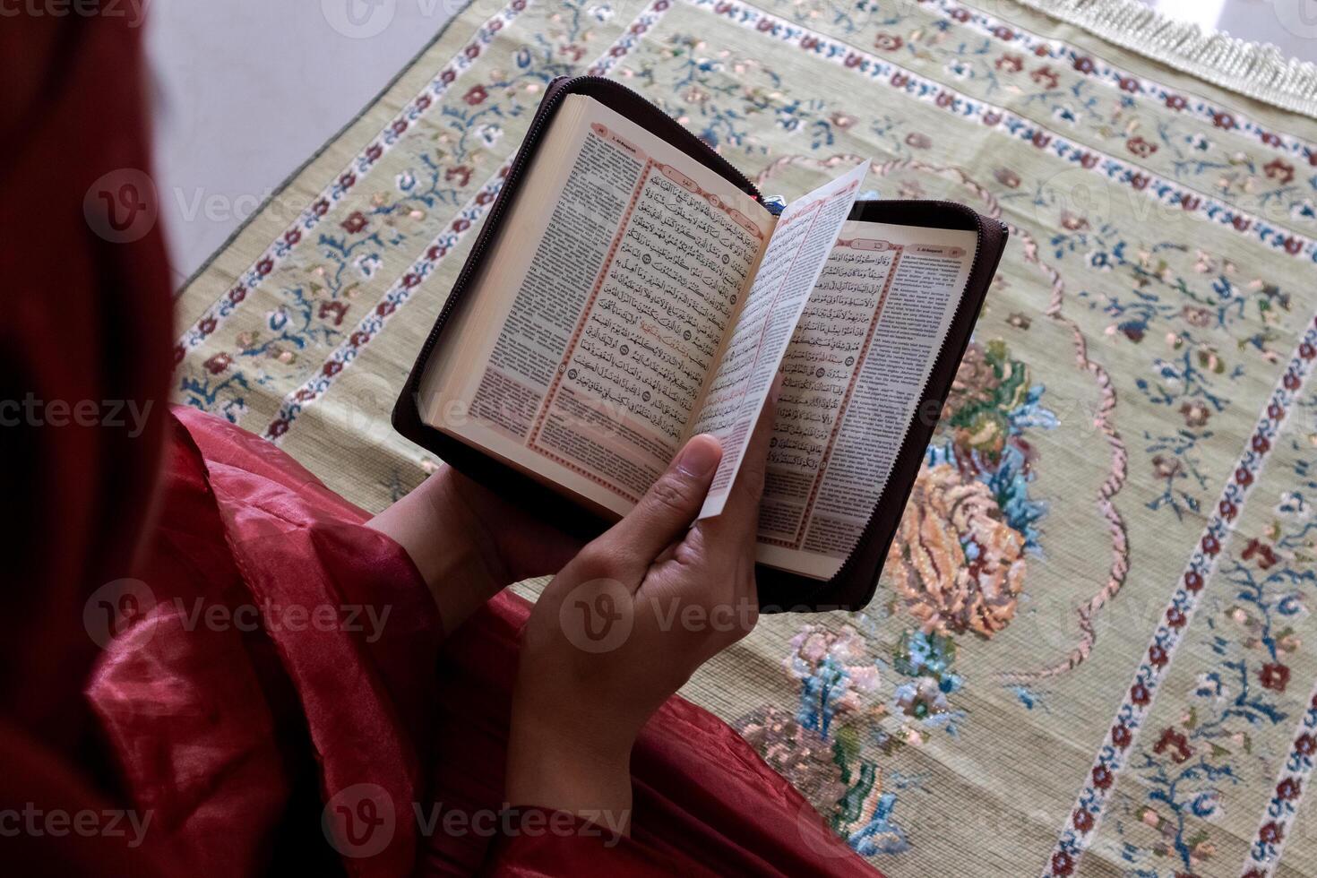 un musulmán mujer sentado en un oración estera y leyendo el Corán con indonesio Traducción foto