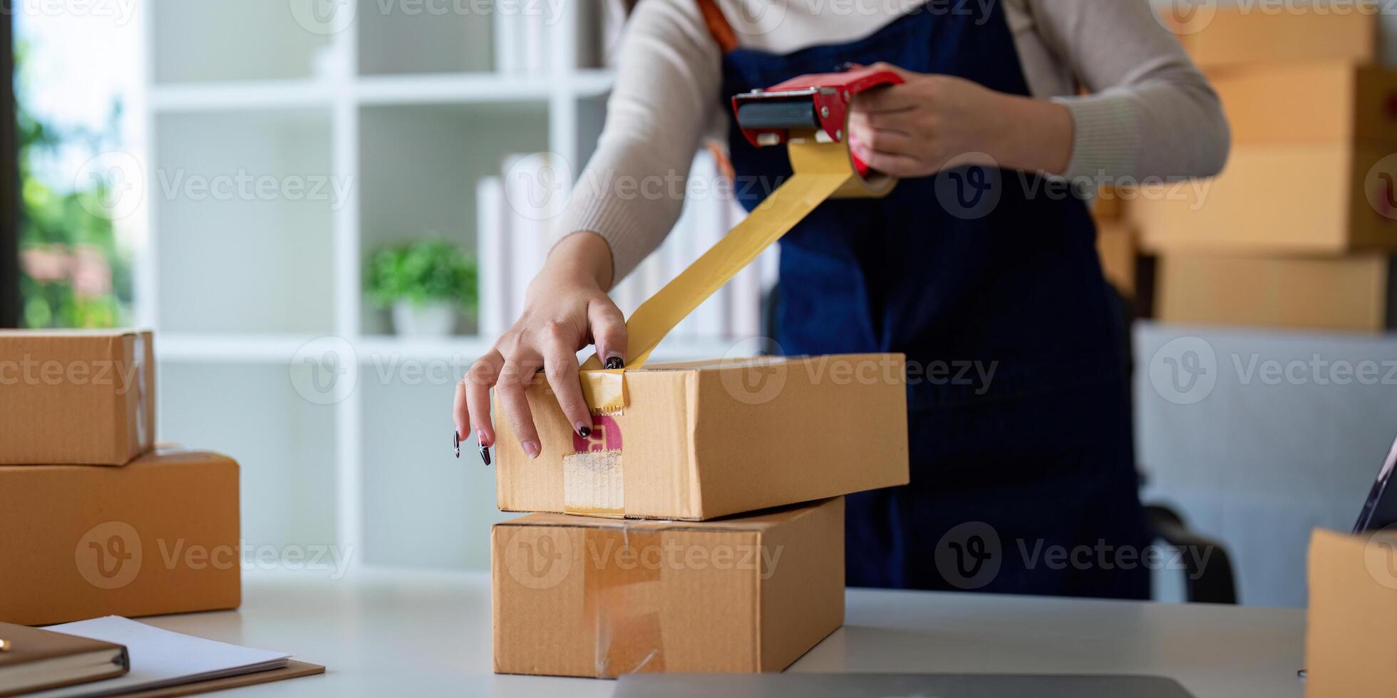 Woman use scotch tape to attach parcel box to prepare goods for the process of packaging, shipping, online sale internet marketing ecommerce concept startup business idea photo