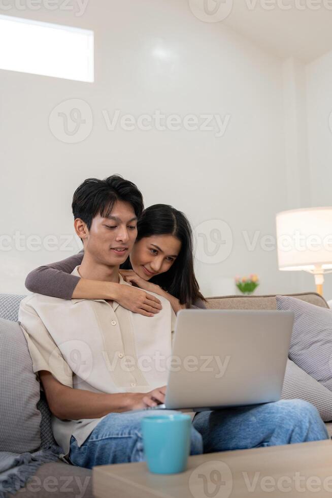 Happy asian couple using laptop sit relax on sofa doing ecommerce shopping online on website at home photo