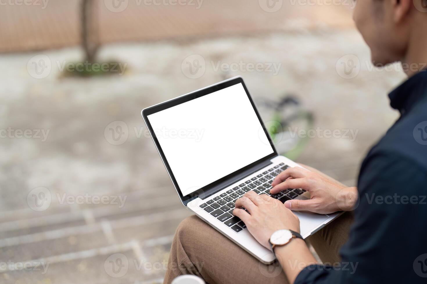 Businessman typing on mockup laptop with blank white screen at urban outside photo