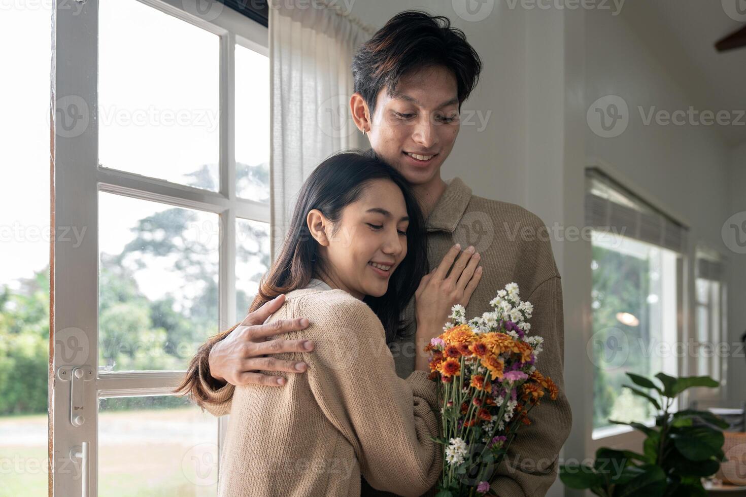 Romantic young asian couple embracing with holding flowers and smiling in living room at home. fall in love. Valentine concept photo