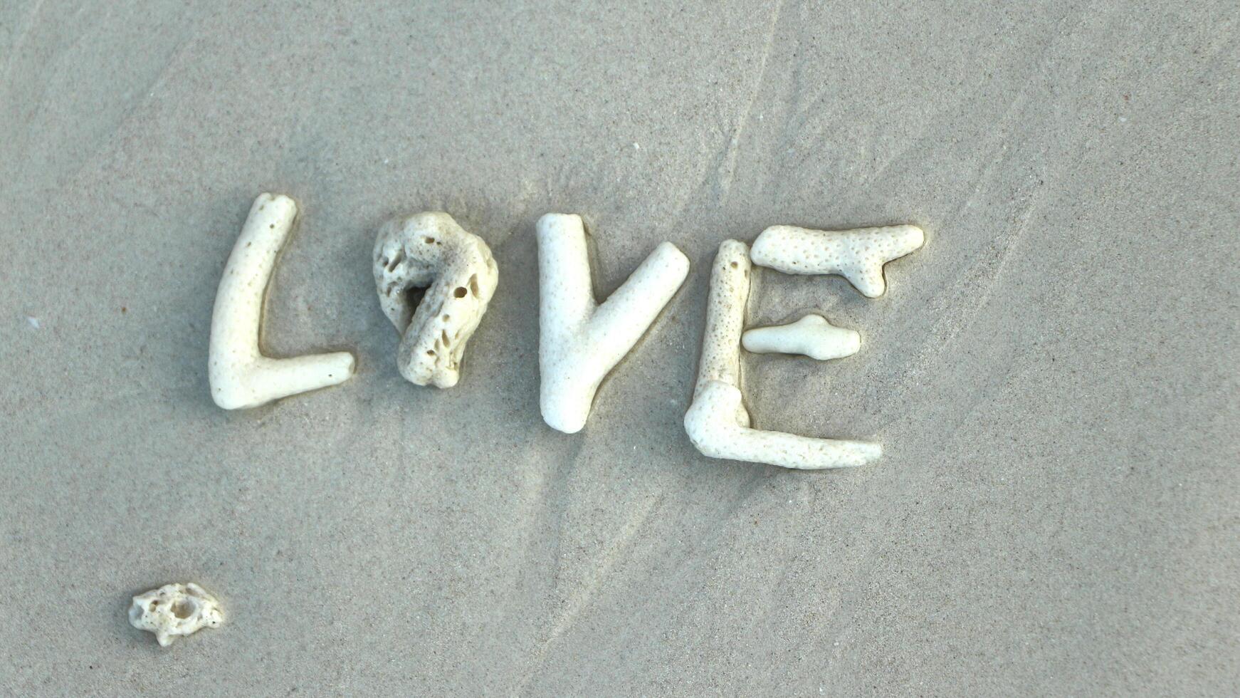 The word love is laid out with corals on a sandy beach. photo