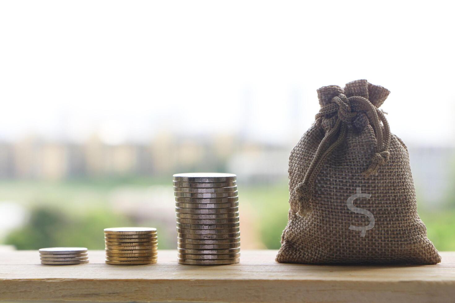 Money bag with stack of coin growing on wooden table on blurred background. photo