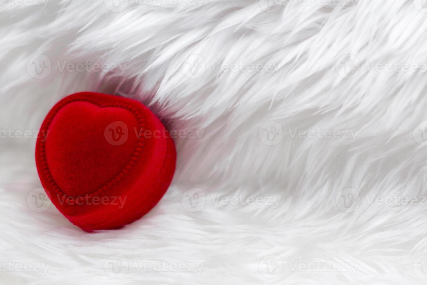 Red heart shaped diamond ring box on fur white blanket. photo