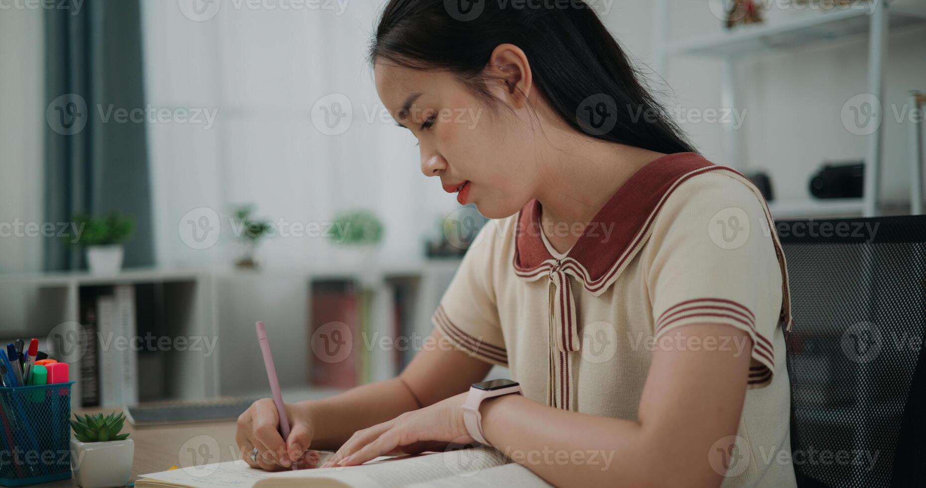 Side view, Selective focus, Female writer sitting at desk writing information on diary notebook while reading book at home, creative thoughts to journaling, idea and inspiration photo