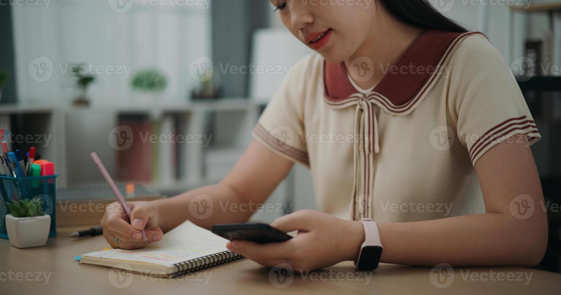 Side view, Selective focus, Female writer sitting at desk writing noting information to diary from smartphone at home, creative thoughts to journaling, idea and inspiration photo
