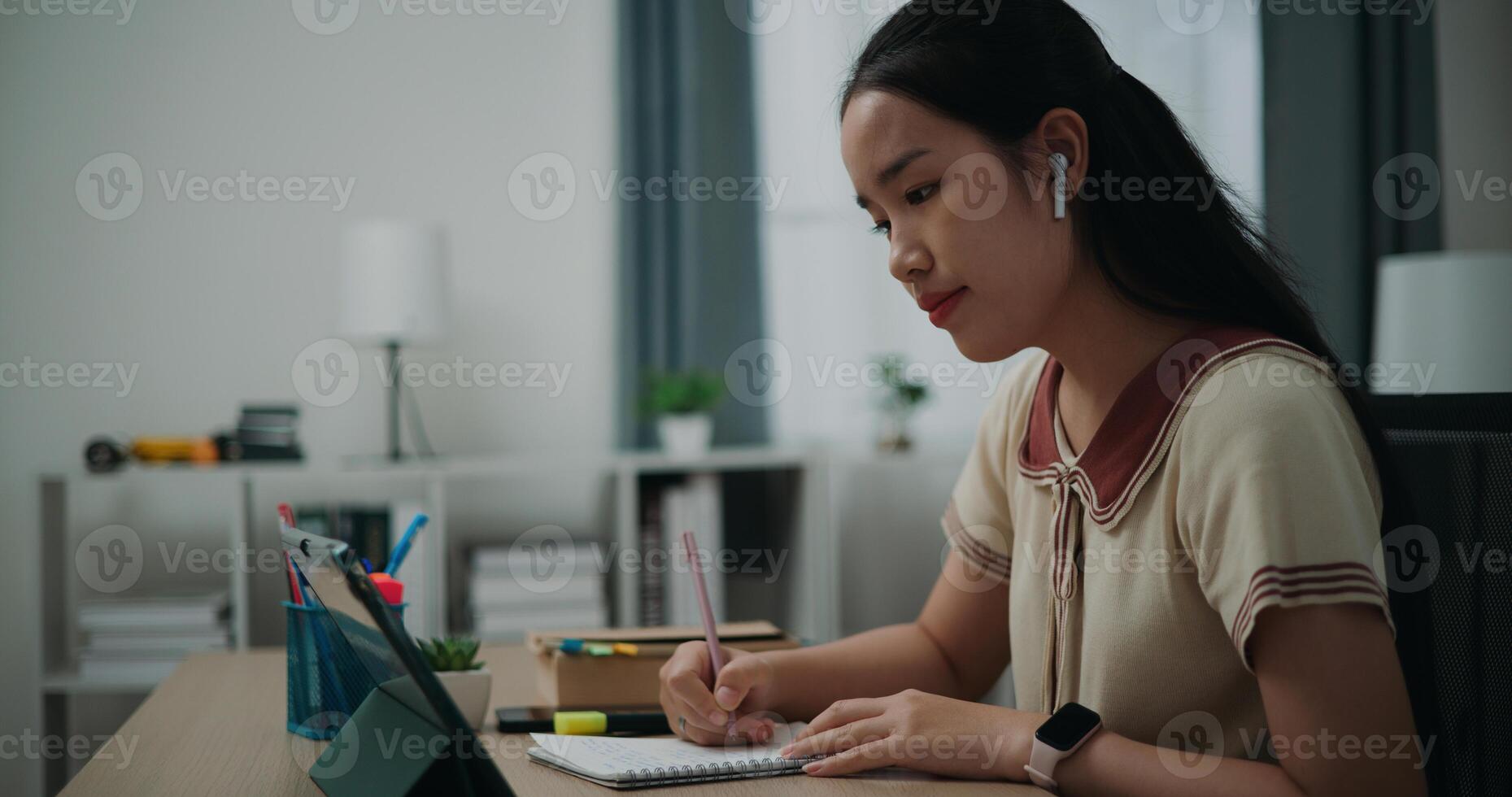 Selective focus, Side view, Female writer wear wireless headphones sitting at desk writing notes while working on tablet for online learning at home, creative thoughts to journaling photo