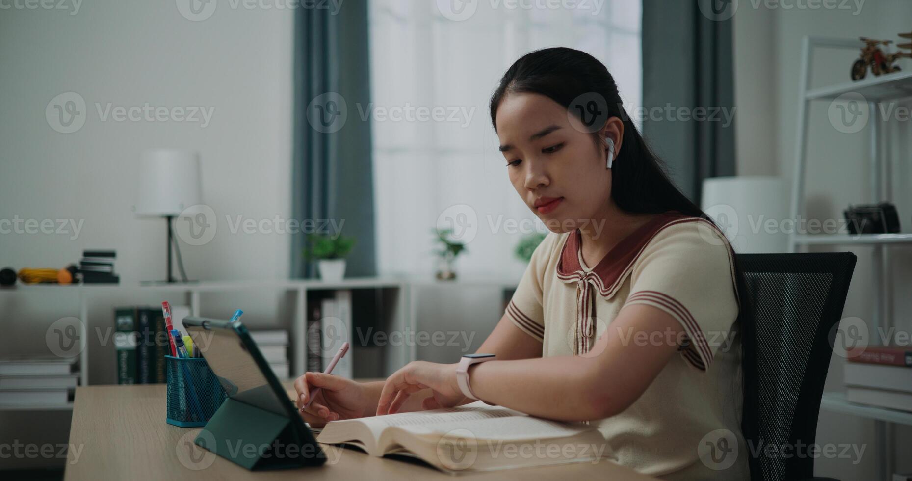 selectivo enfocar, lado vista, hembra inalámbrico auriculares escritor sentado a escritorio escritura información en diario cuaderno mientras leyendo libro a hogar, creativo pensamientos a diario, idea y inspiración foto