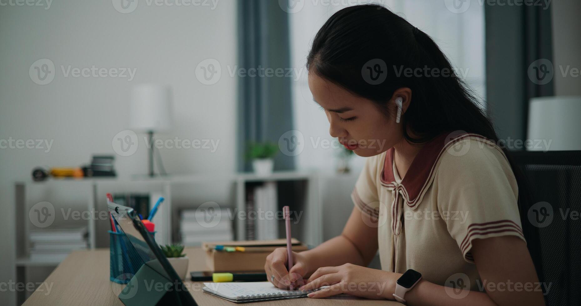 Selective focus, Side view, Female writer wear wireless headphones sitting at desk writing notes while working on tablet for online learning at home, creative thoughts to journaling photo