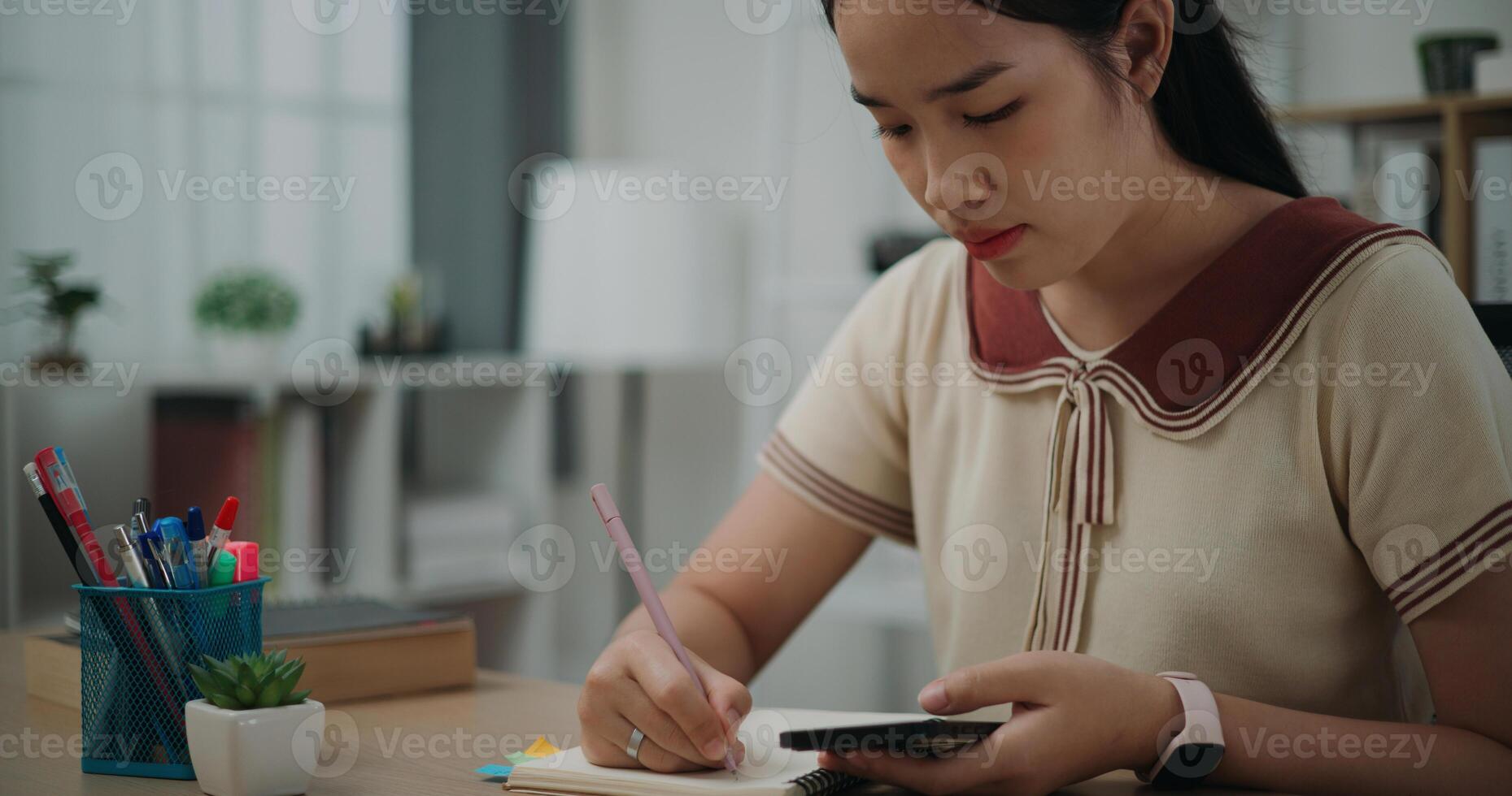 Selective focus, Female writer sitting at desk writing noting information to diary from smartphone at home, creative thoughts to journaling, idea and inspiration photo