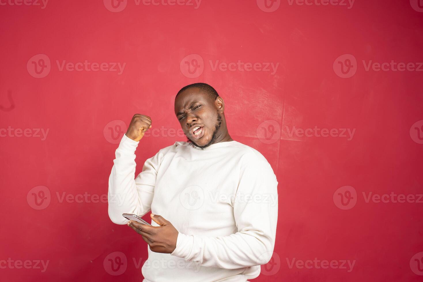 lleno de alegría africano hombre utilizando teléfono inteligente Deportes apuesta, ganar dinero aislado en rojo antecedentes. foto