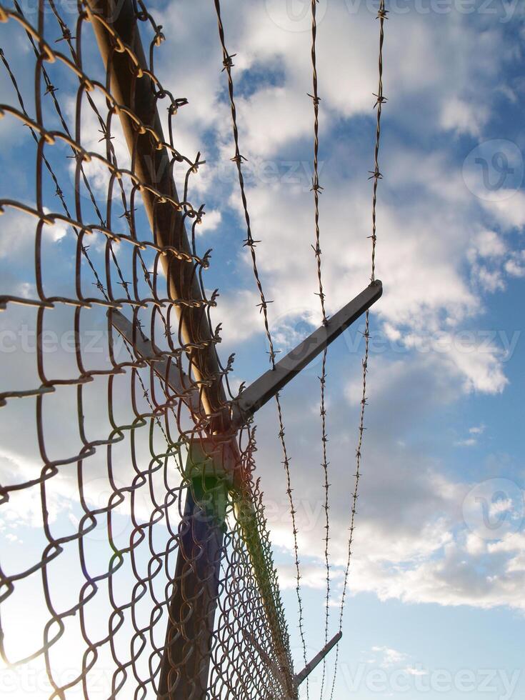 Fence with barbed wire against sky and clounds photo