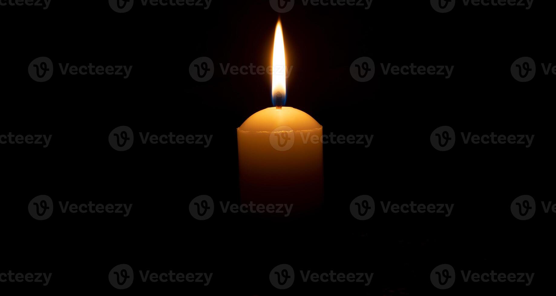 Single burning candle flame or light glowing on a big white candle on black or dark background on table in church for Christmas, funeral or memorial service with copy space. photo