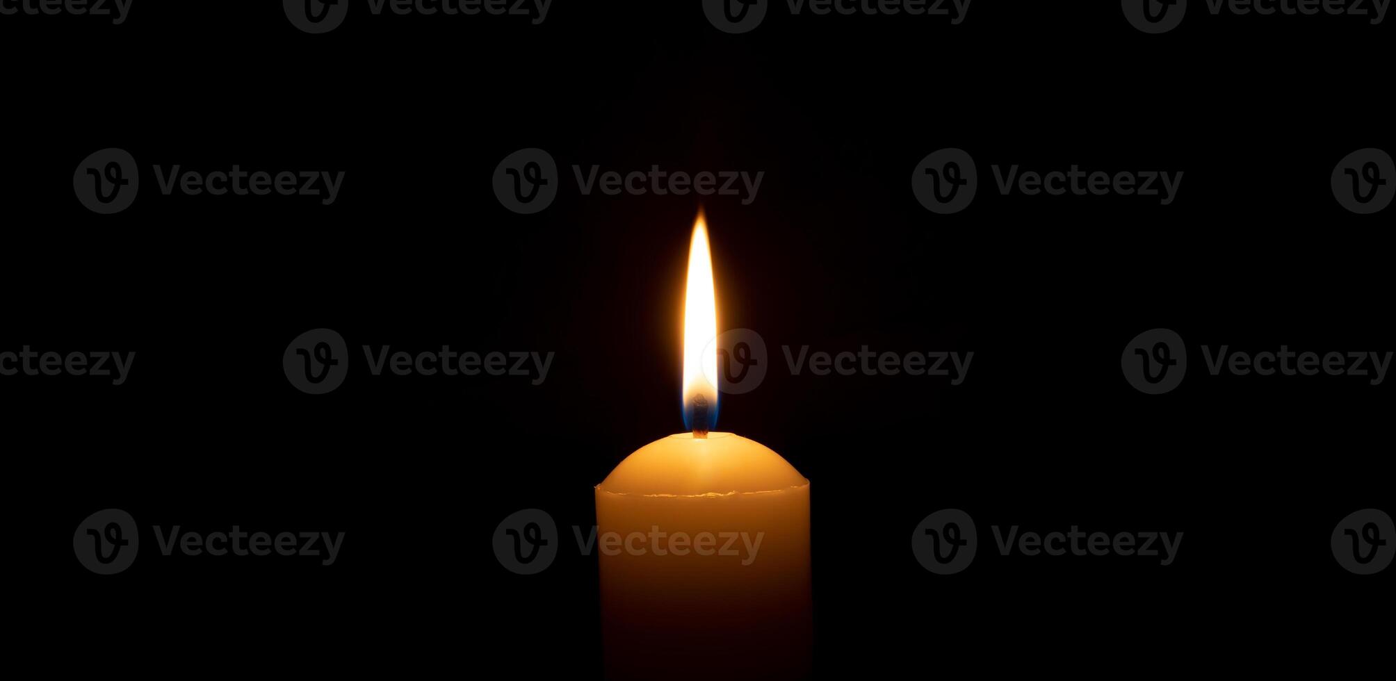 Single burning candle flame or light glowing on a big white candle on black or dark background on table in church for Christmas, funeral or memorial service with copy space. photo