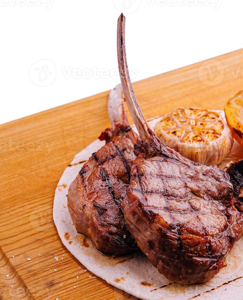 Grilled lamb chops on wooden board with herbs and spices photo