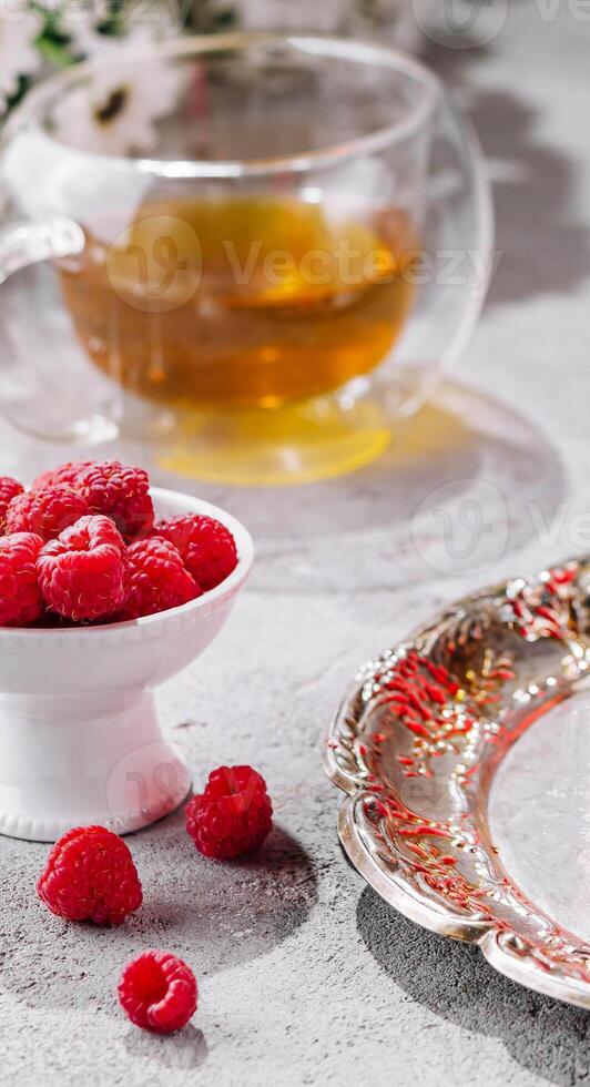 raspberries in a bowl and a glass cup of tea photo