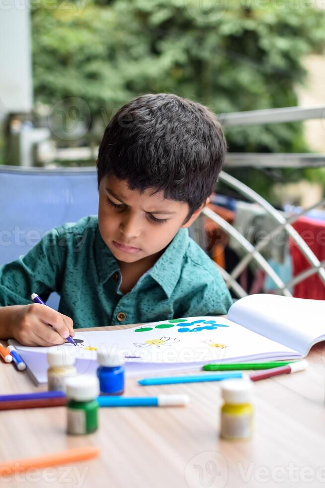 inteligente indio pequeño chico realizar pulgar pintura con diferente vistoso agua color equipo durante el verano vacaciones, linda indio niño haciendo vistoso pulgar pintura dibujo en de madera mesa foto