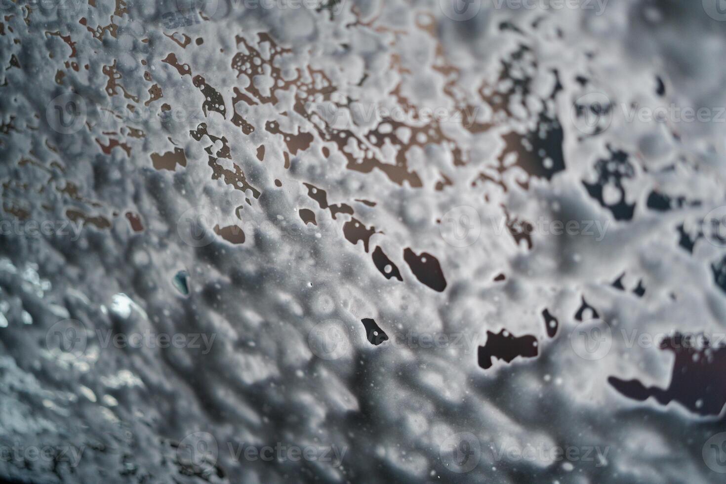 Car running through an automatic car wash with foam on glass. Abstract wet windshield background. photo