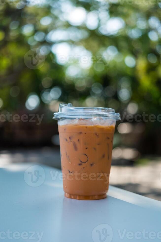 Ice Thai milk tea in a plastic cup on wooden table against a natural background. photo