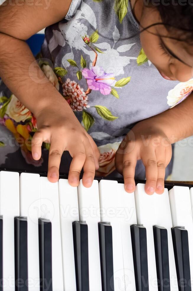 Asian cute girl playing the synthesizer or piano. Cute little kid learning how to play piano. Child's hands on the keyboard indoor. photo