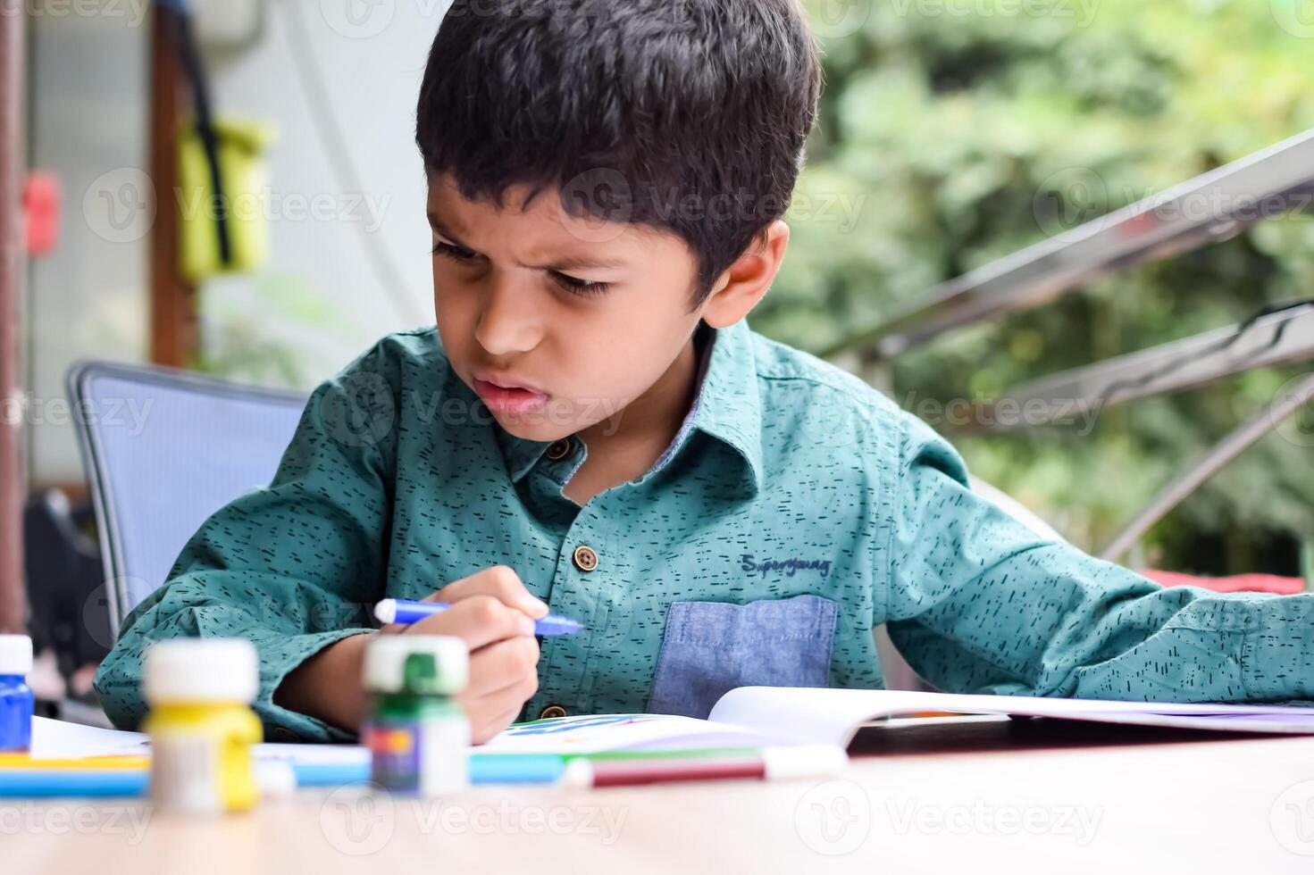 inteligente indio pequeño chico realizar pulgar pintura con diferente vistoso agua color equipo durante el verano vacaciones, linda indio niño haciendo vistoso pulgar pintura dibujo en de madera mesa foto