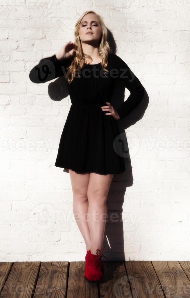 Plump Caucasian Blond Woman Black Dress White Wall photo