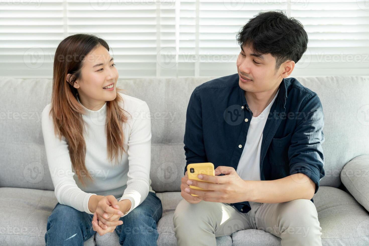 Asian couple smiling and happily use smartphone to online shopping. Husband ready to pay birthday present for beautiful wife. Find accommodation online for honeymoon, App online, book flight ticket photo