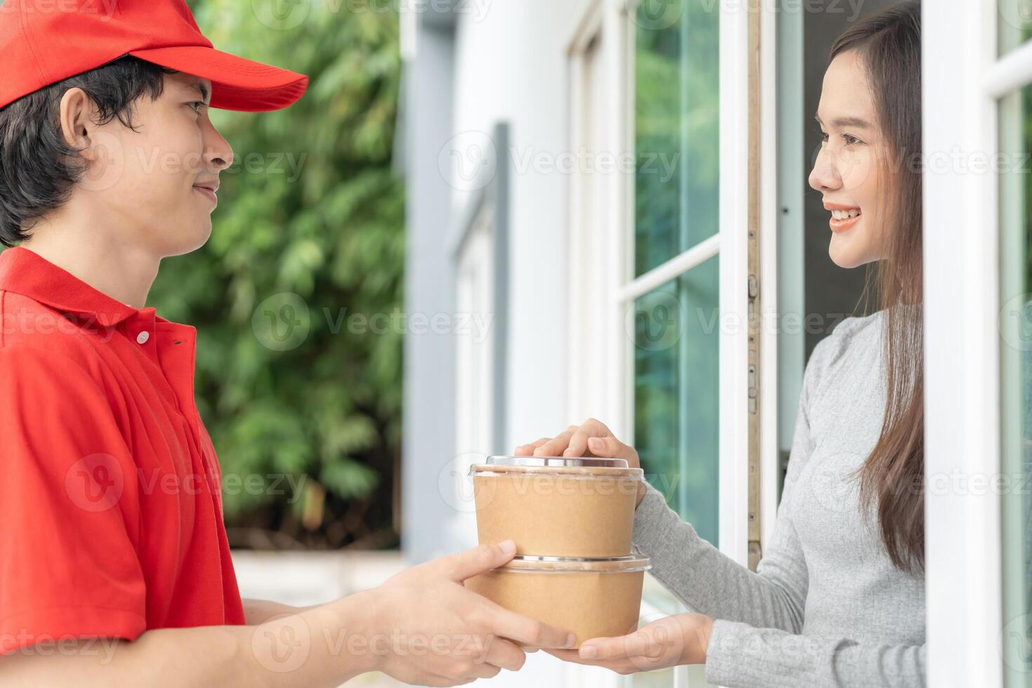 Happy smiling Asian woman receives paper box parcel of food from courier front house. Delivery man send deliver express. online shopping, paper container, takeaway, postman, delivery service, packages photo