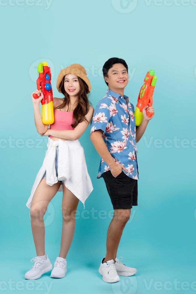 asiático Pareja en verano ropa con agua pistola en estudio azul antecedentes. ellos sonrisa y Mira a el cámara a el Songkran festival en tailandia foto