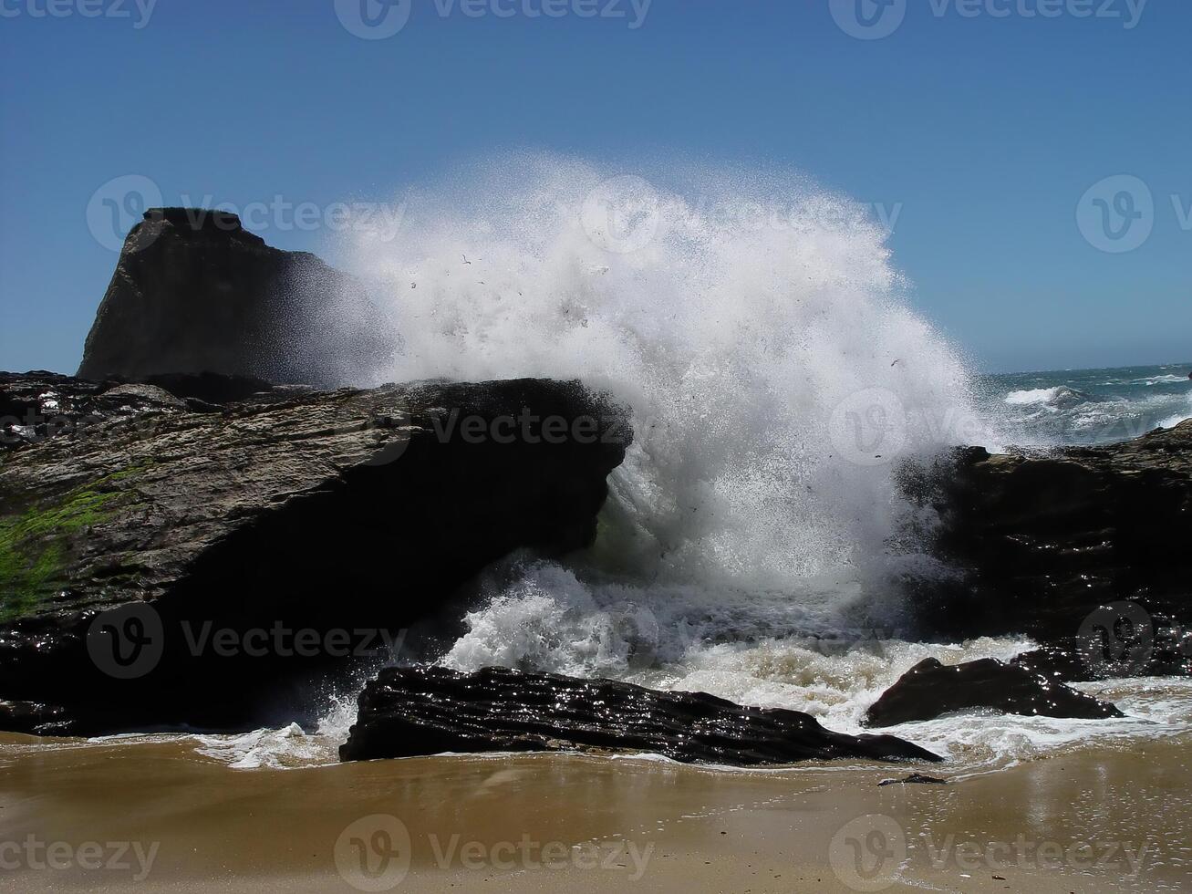 Wave Crashing Over Rocks On Sandy Beach Blue Sky photo